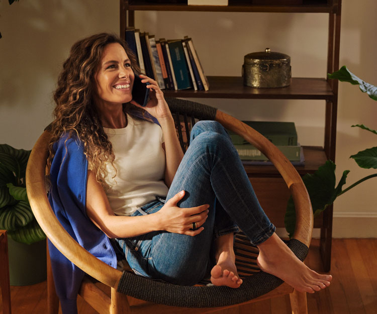 chica sonriente, sentada comodamente en una silla moderna, hablando por teléfono